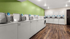 A laundry facility with multiple washing machines and dryers, a green wall, and a wooden floor.