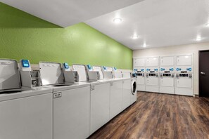 Een wasserette met meerdere wasmachines en drogers, een groene wand en een houten vloer.