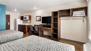Una habitación compacta con dos camas, un kitchenette, un escritorio y un televisor.
