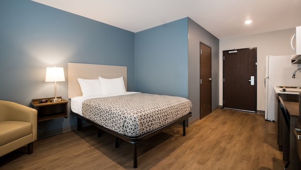 A hotel room with a bed, bedside table, lamp, and a small desk with a chair.