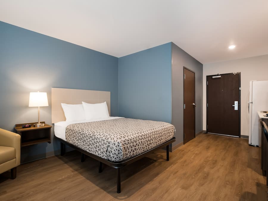 A hotel room with a bed, bedside table, lamp, and a small desk with a chair.