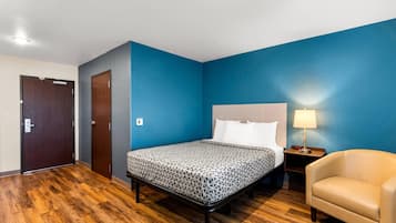 Una habitación de hotel con una cama, mesita de noche, lámpara, silla y una puerta.