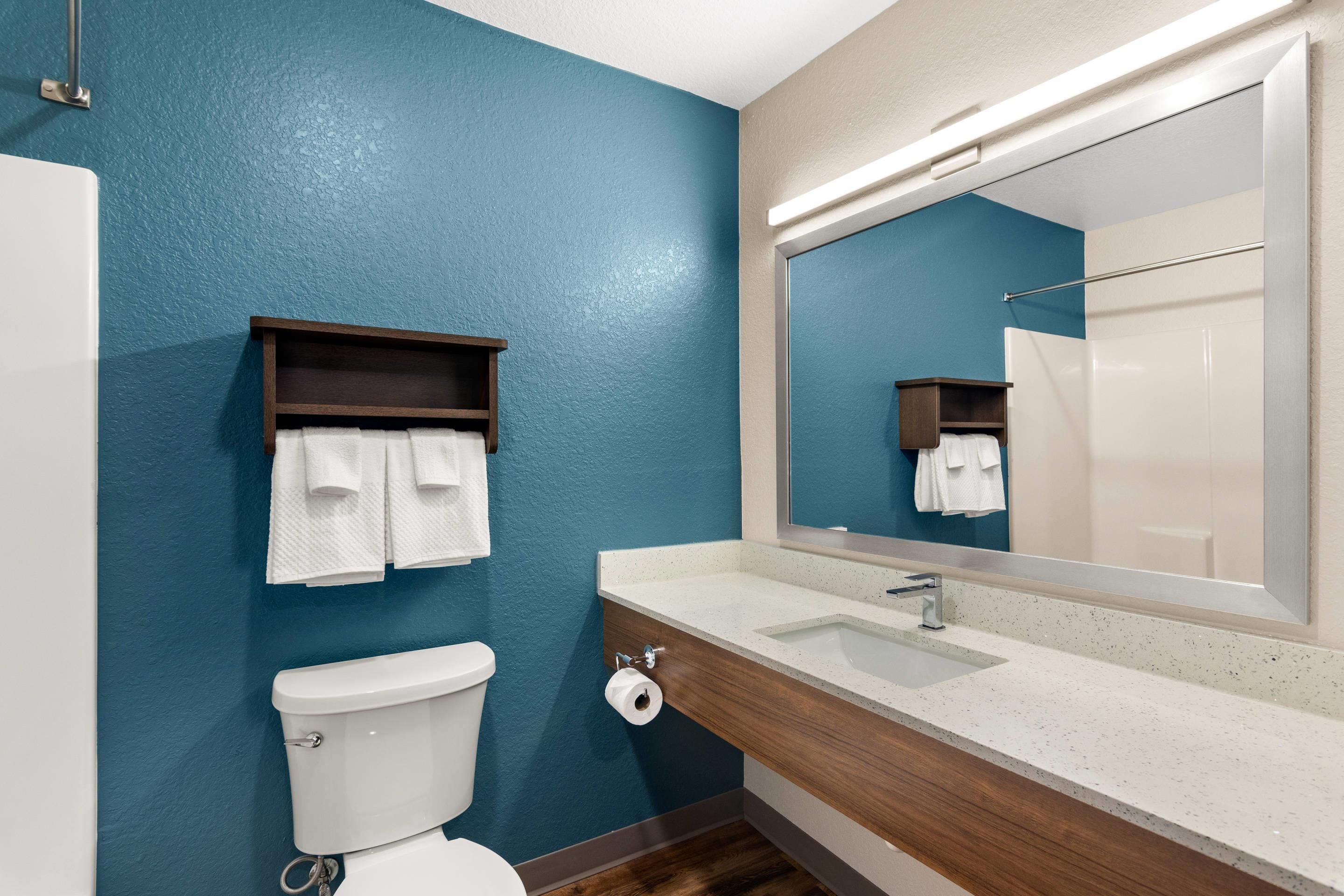 Un bagno con un WC bianco, un lavandino con uno specchio sopra e due portasci con asciugamani bianchi.