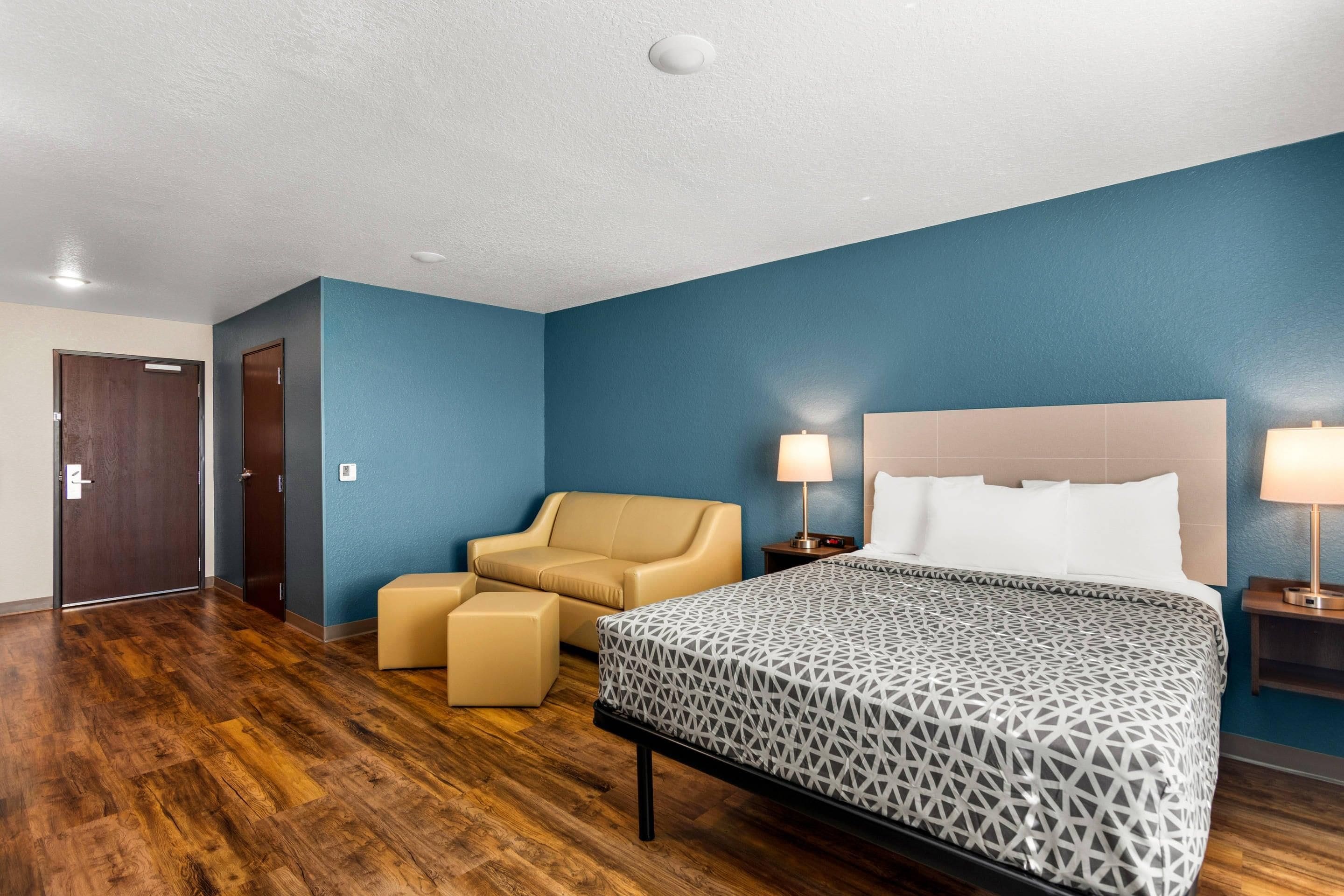 Una habitación de hotel con cama, una silla, una mesita y una mesita de noche.