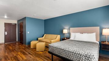 Una habitación de hotel con cama, una silla, una mesita y una mesita de noche.