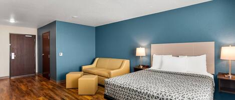 Una habitación de hotel con cama, una silla, una mesita y una mesita de noche.