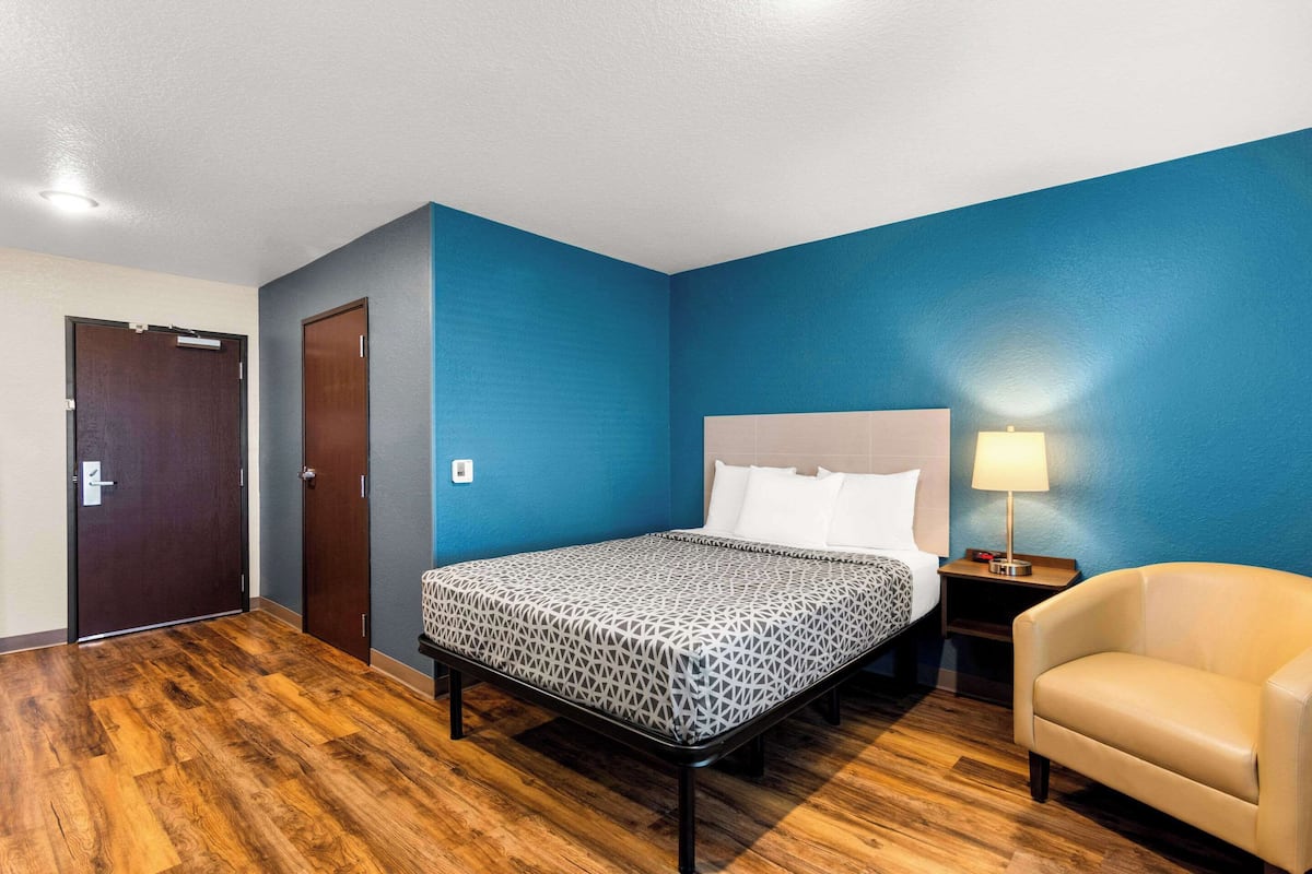 Una habitación de hotel con una cama, una silla, una mesita de noche y una puerta.