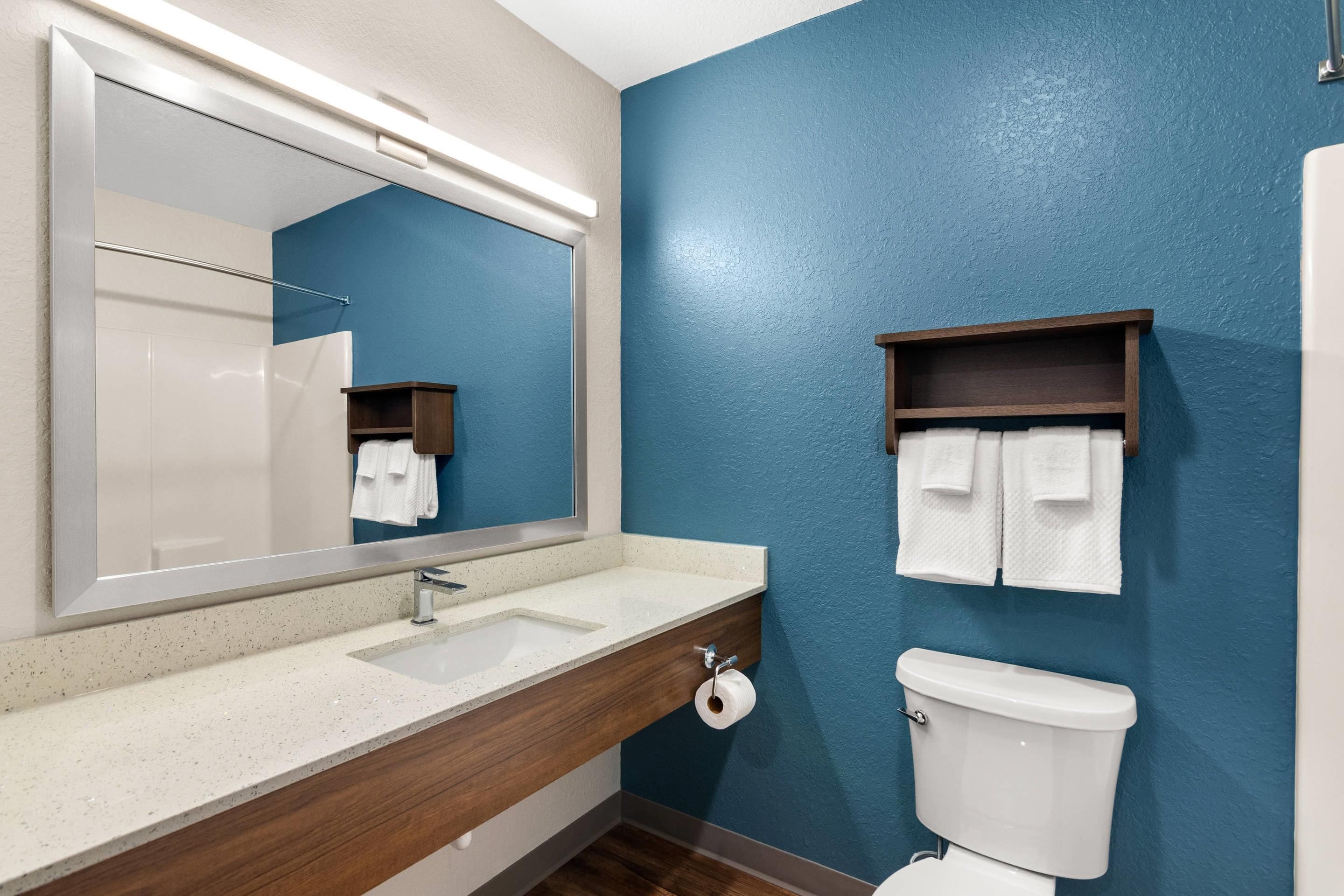 A bathroom with a white sink, mirror, and toilet, with blue walls and a wooden vanity.