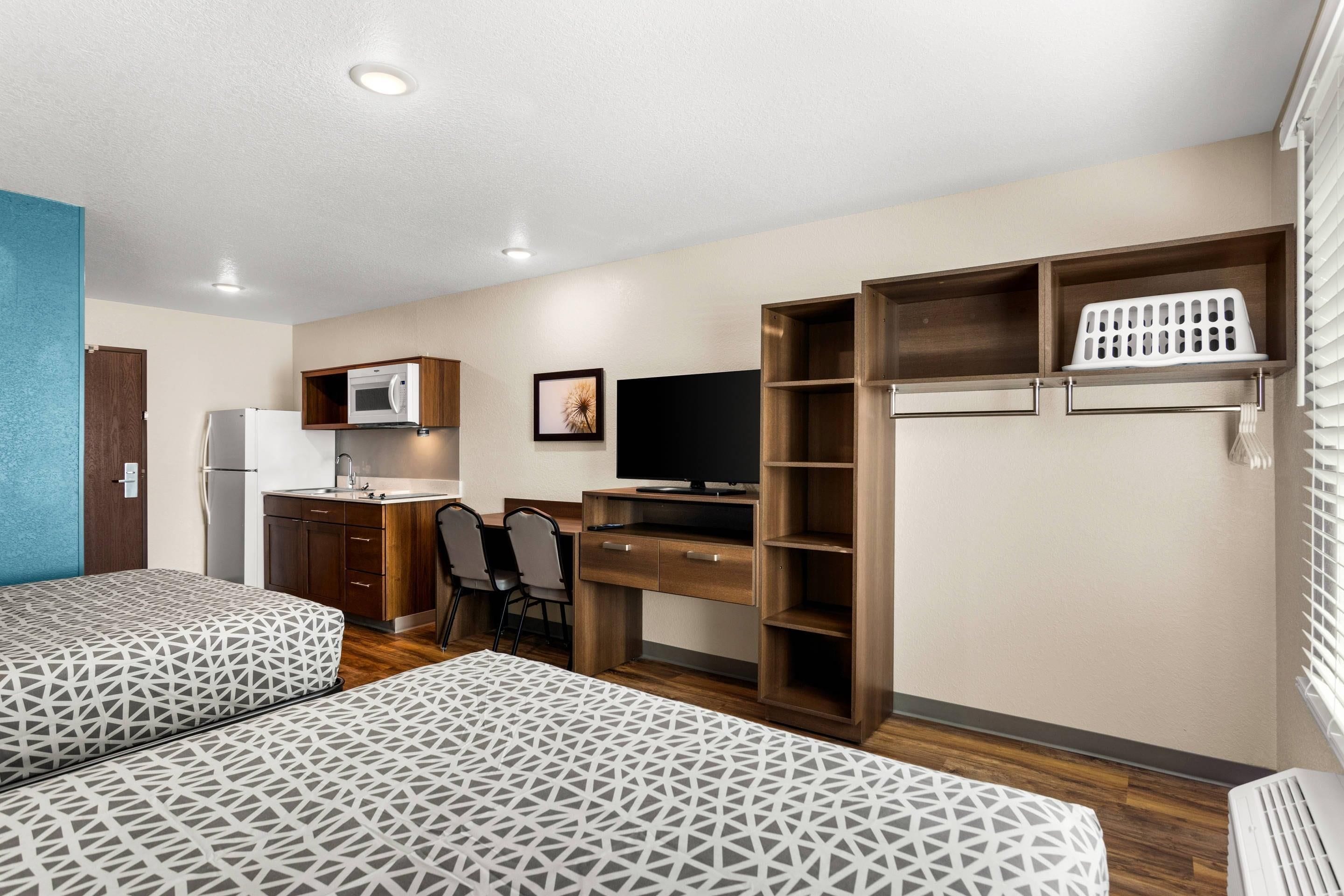A compact room with two beds, a kitchenette, a desk with a computer, and a television.