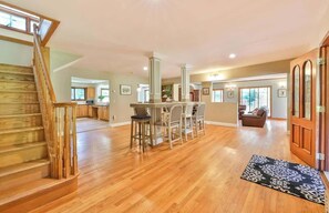 A spacious living area with a wooden staircase, a kitchen, and a dining area with bar stools.