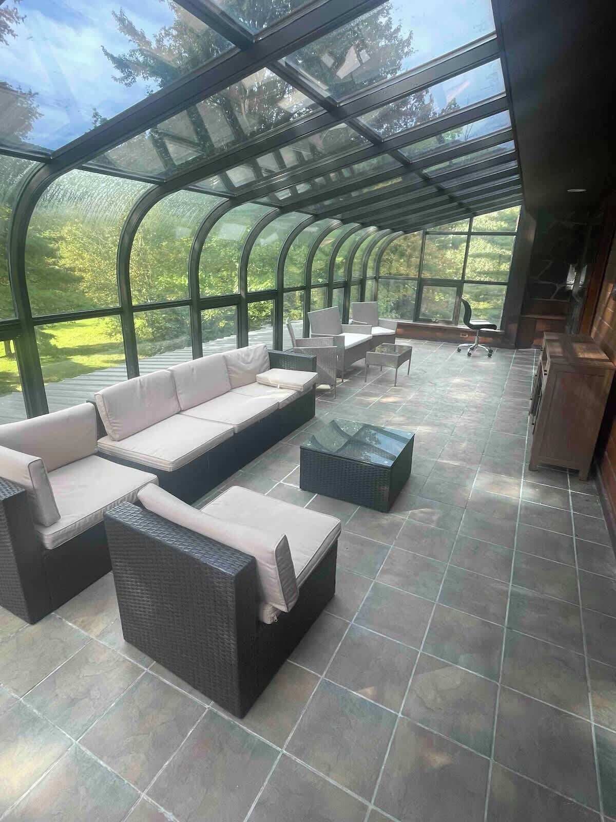 A covered outdoor seating area with a curved glass roof, wicker furniture, and a view of the surrounding greenery.
