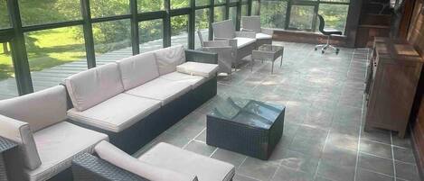 A covered outdoor seating area with a curved glass roof, wicker furniture, and a view of the surrounding greenery.