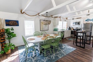 Un comedor con una mesa blanca, sillas verdes y un tapete azul estampado.