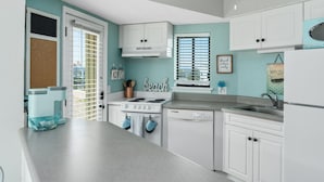 Una cocina moderna con armarios blancos, una estufa y un lavavajillas. Hay una ventana con persianas y un cartel que dice 'Good vibes only'.