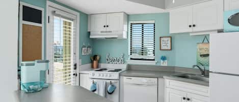 A modern kitchen with white cabinetry, a stove, and a dishwasher. There is a window with blinds and a sign that says "Good vibes only."