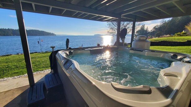 Un jacuzzi bajo una zona cubierta con vista a un lago y montañas lejanas.