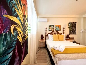 Habitación de hotel con cama, mesita de noche, lámpara y aire acondicionado instalado en la pared.