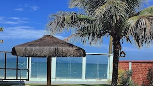 Une structure en forme de parasol recouverte de chaume, un palmier et une vue sur l’océan.