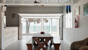 Une pièce spacieuse avec une grande table, un canapé en osier et une vue sur la mer.