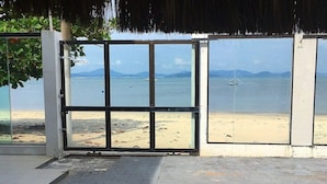 Une vue sur la plage à travers une porte vitrée, un chemin de pierres et une zone herbeuse.
