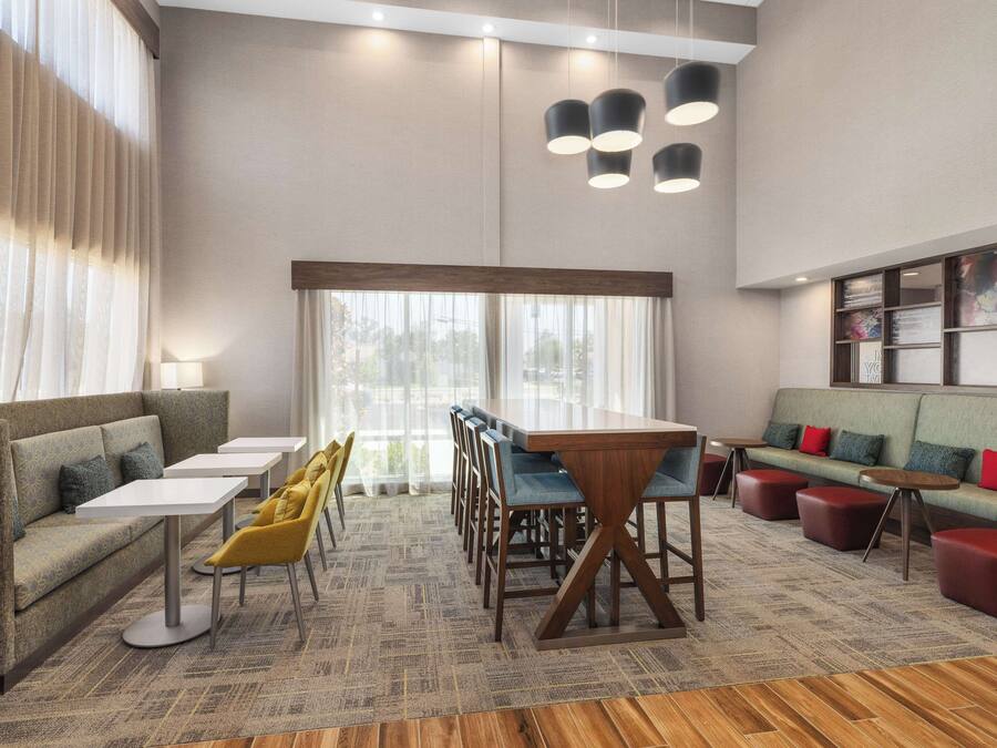 Eine moderne Hotelhalle mit einem langen Esstisch, mehreren Stühlen, einer Couch und einer Sitzecke mit roten Kissen.