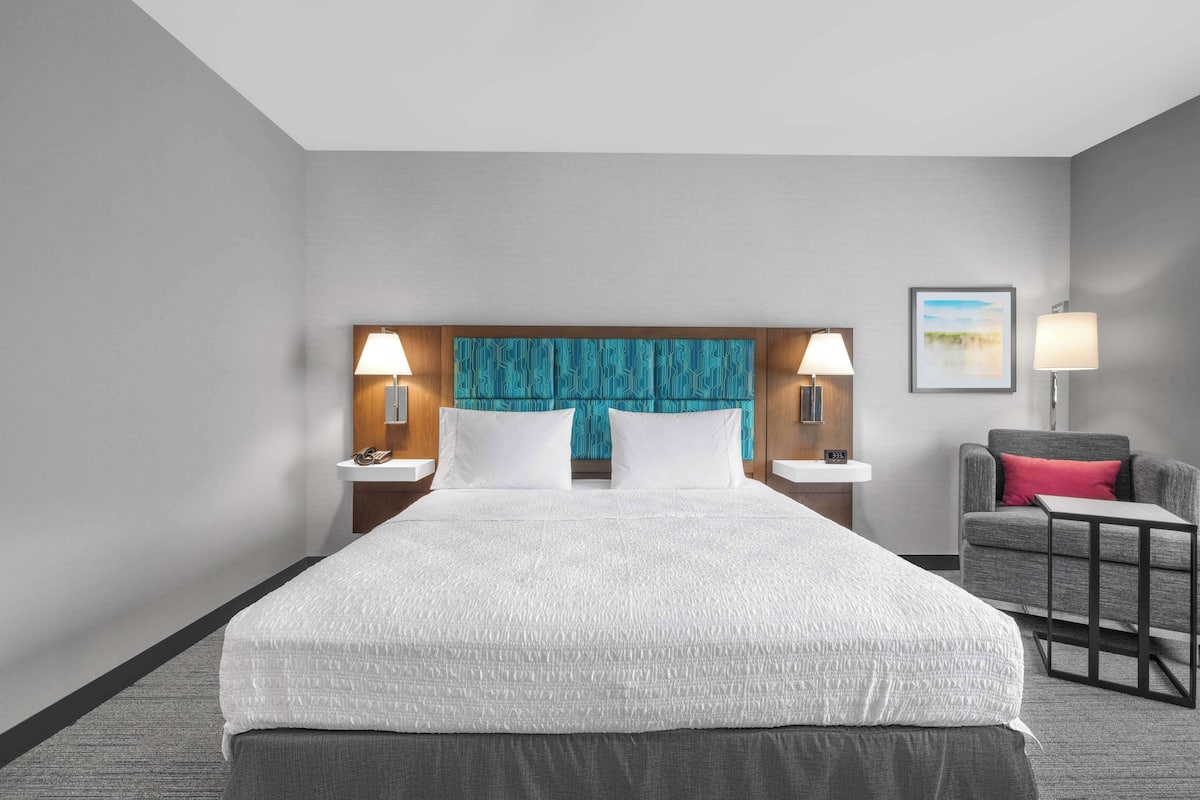 A hotel room with a large bed, two bedside tables with lamps, a chair, and a small table.