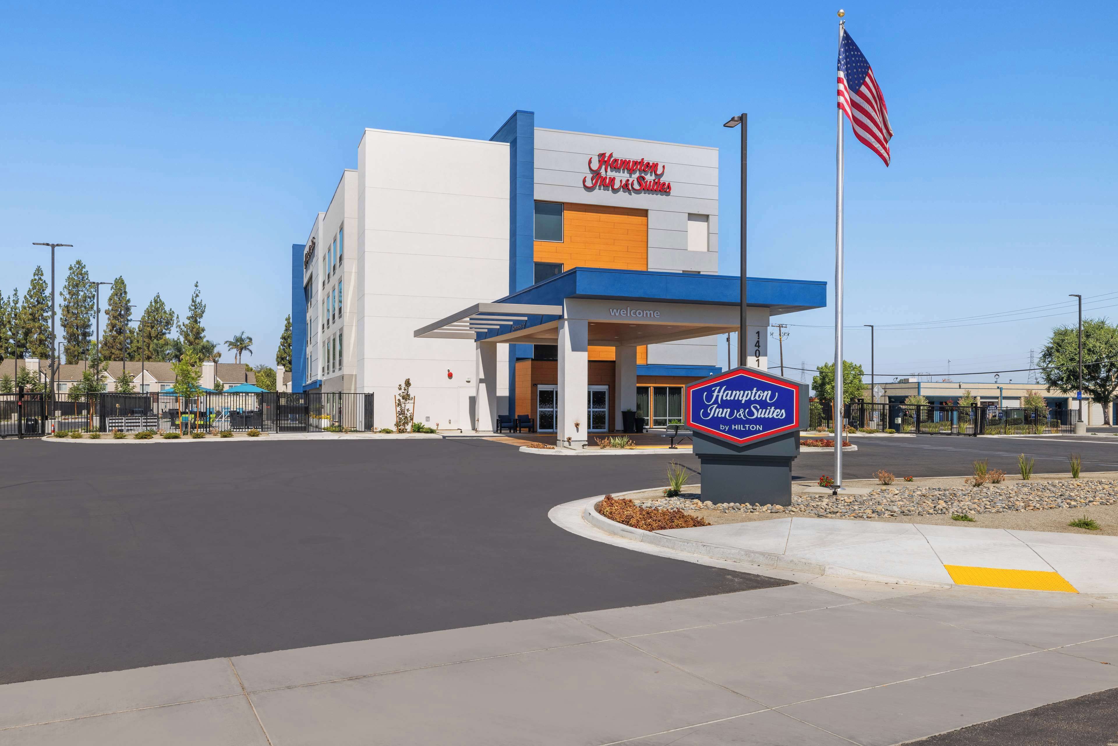 Un hôtel Hampton Inn & Suites doté d’une façade moderne, d’une entrée accueillante et arborant le drapeau américain.