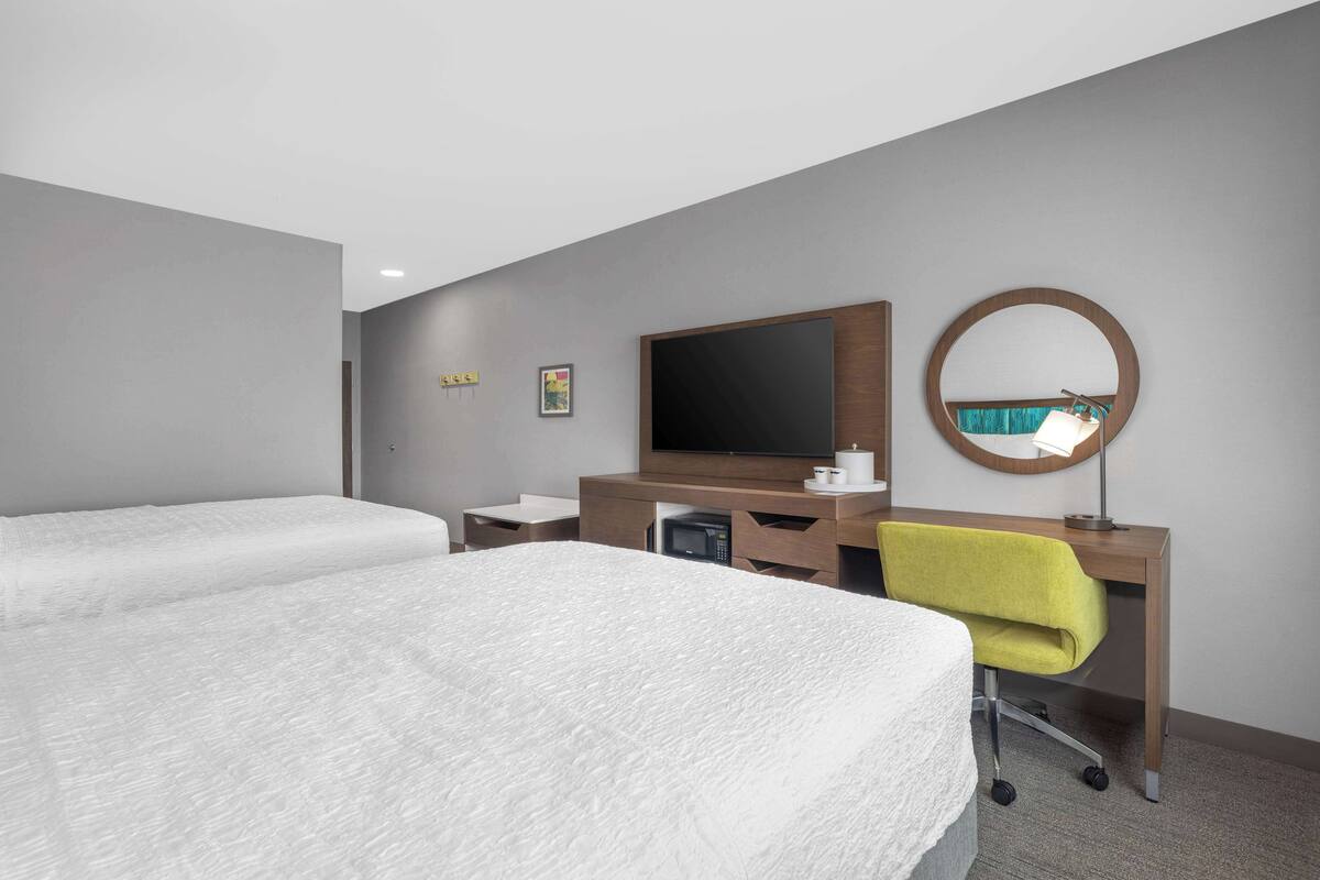 A hotel room with two beds, a desk with a computer, a TV, and a mirror.