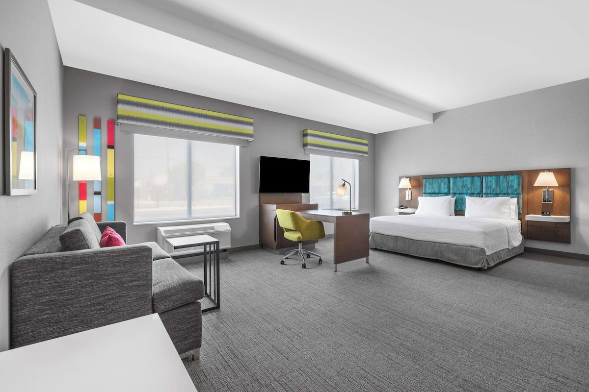 A hotel room with a bed, a desk, a chair, a TV, and a window with blinds.