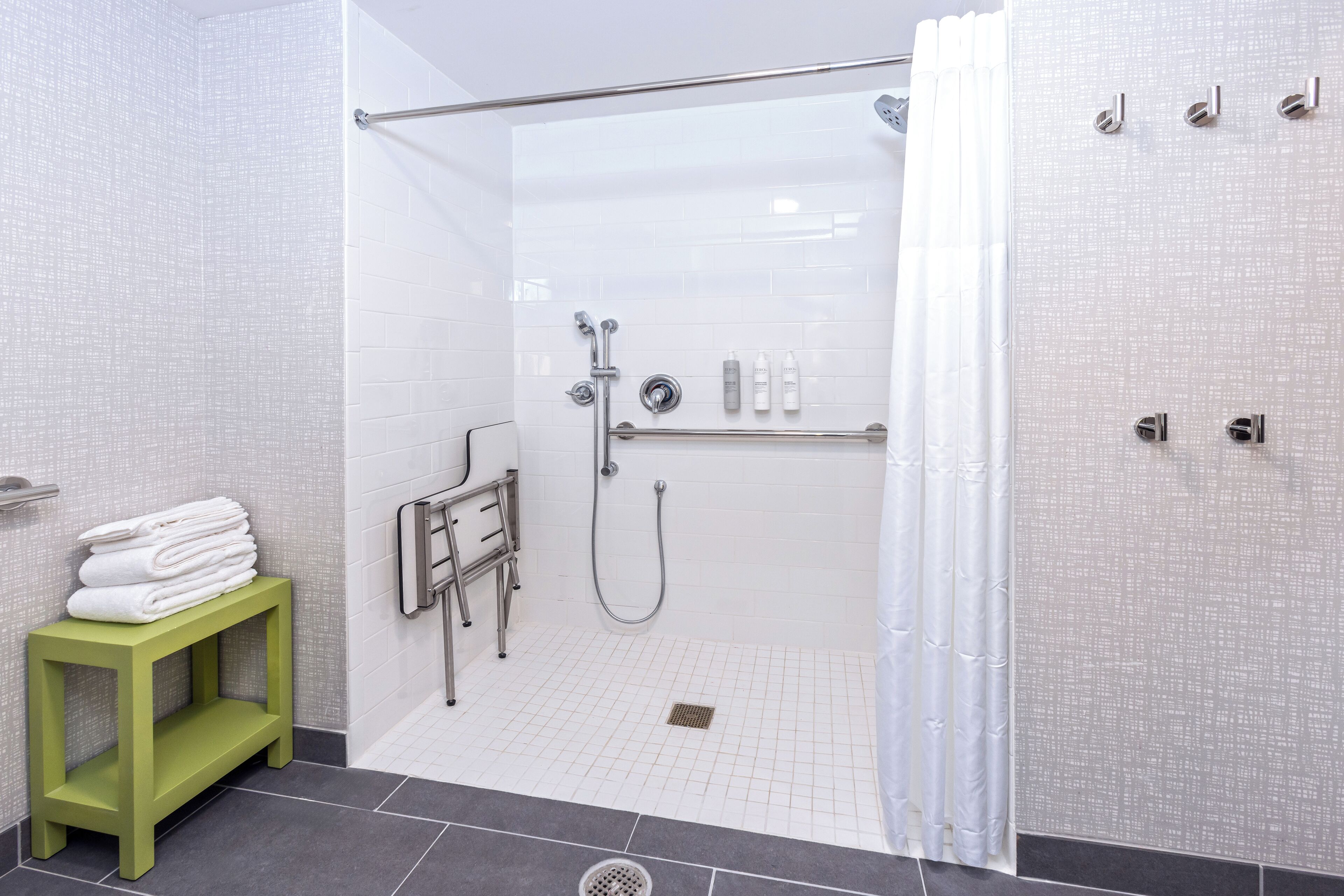 A modern shower area with a glass door, a towel rack, and a green stool.