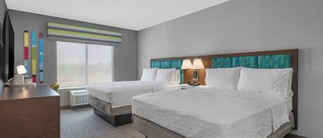 Een hotelkamer met twee bedden, een bureau, een stoel, een televisie en een raam met jaloezieën.