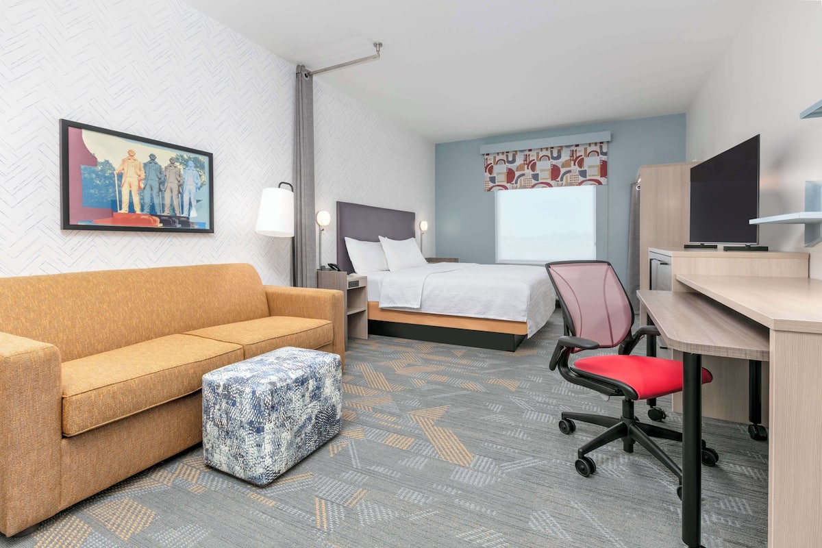 A hotel room with a bed, a sofa, a desk, a chair, and a television.