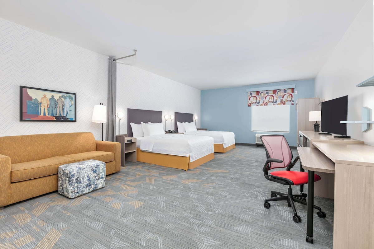 A hotel room with two beds, a desk, a chair, a sofa, and a patterned carpet.