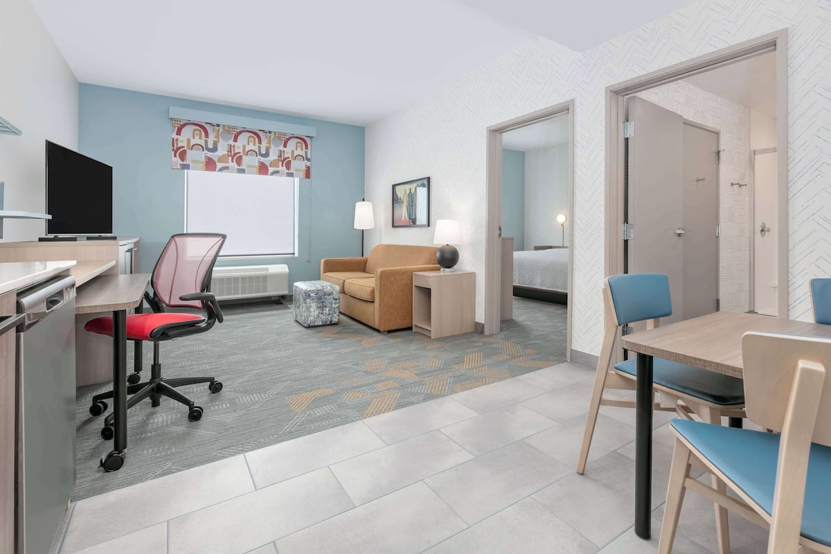A modern hotel room with a desk, office chair, sofa, and a dining table with chairs.