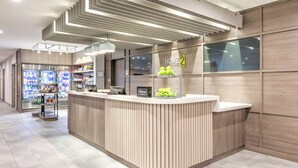 Zona de recepción moderna de hotel, con un mostrador de madera, un minibar y vistas al vestíbulo.