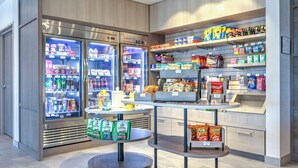 Un quiosco autoservicio de bebidas y snacks, con dispensadores de bebidas frías, una variedad de productos y una caja de cobro.