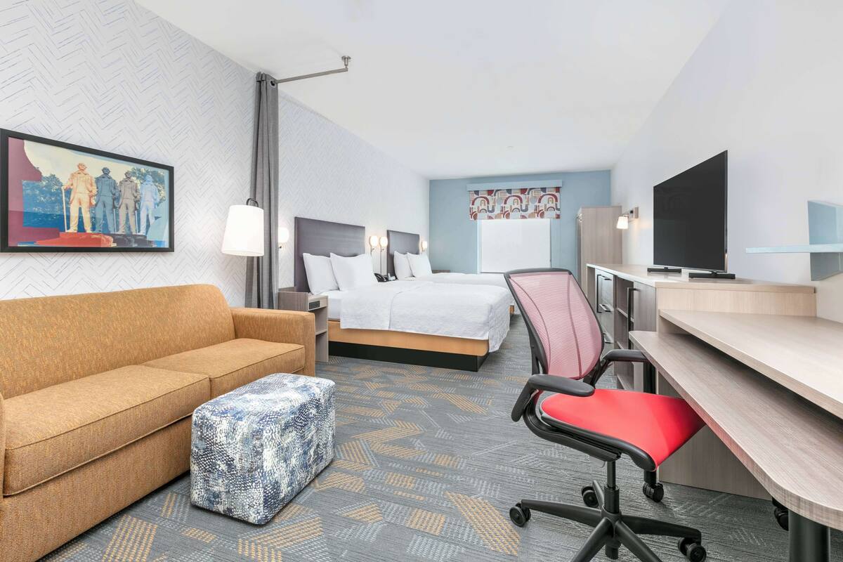A hotel room with a sofa, a bed, a desk, a chair, a television, and a painting on the wall.