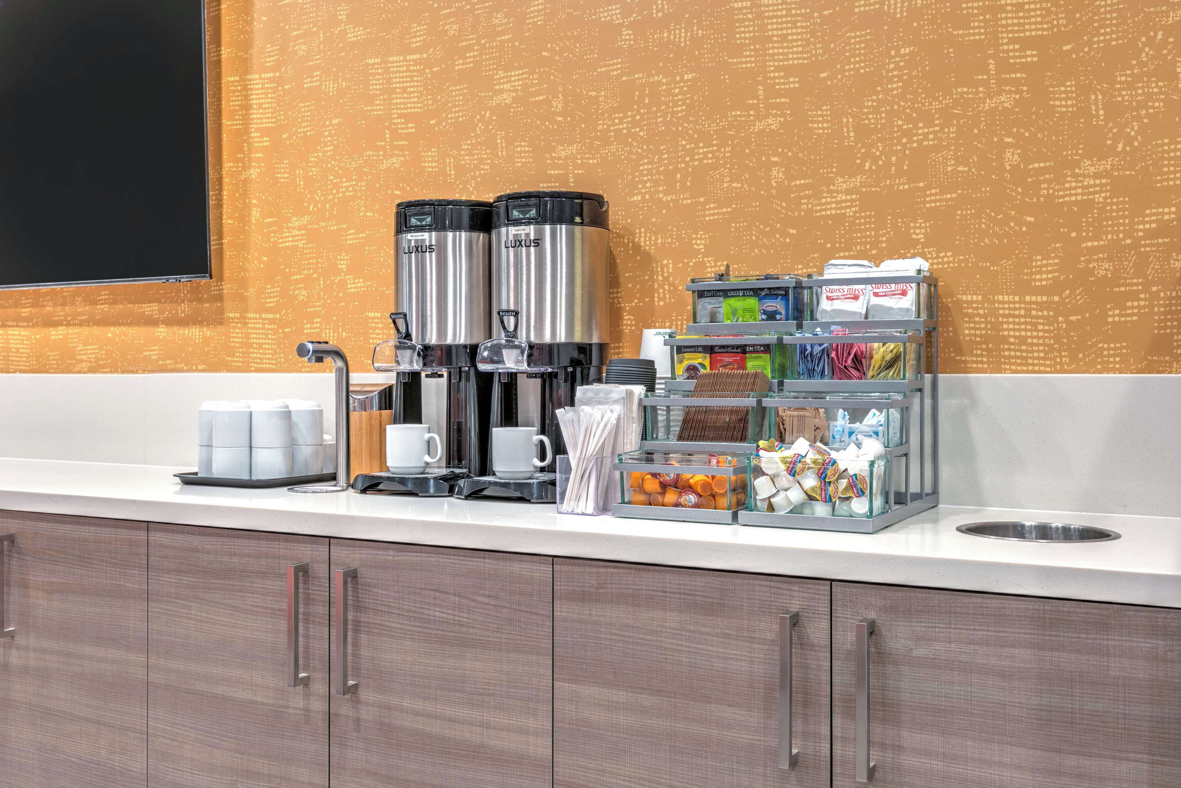 A modern coffee station with two coffee makers, a coffee pot, and a variety of coffee pods and supplies.