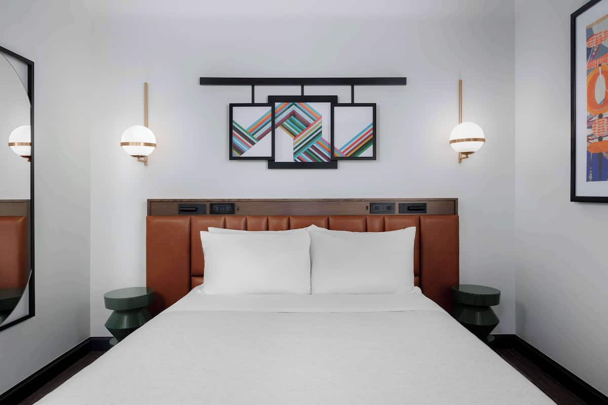 A hotel room with a large bed, two bedside tables, a headboard, and three framed artworks on the wall.