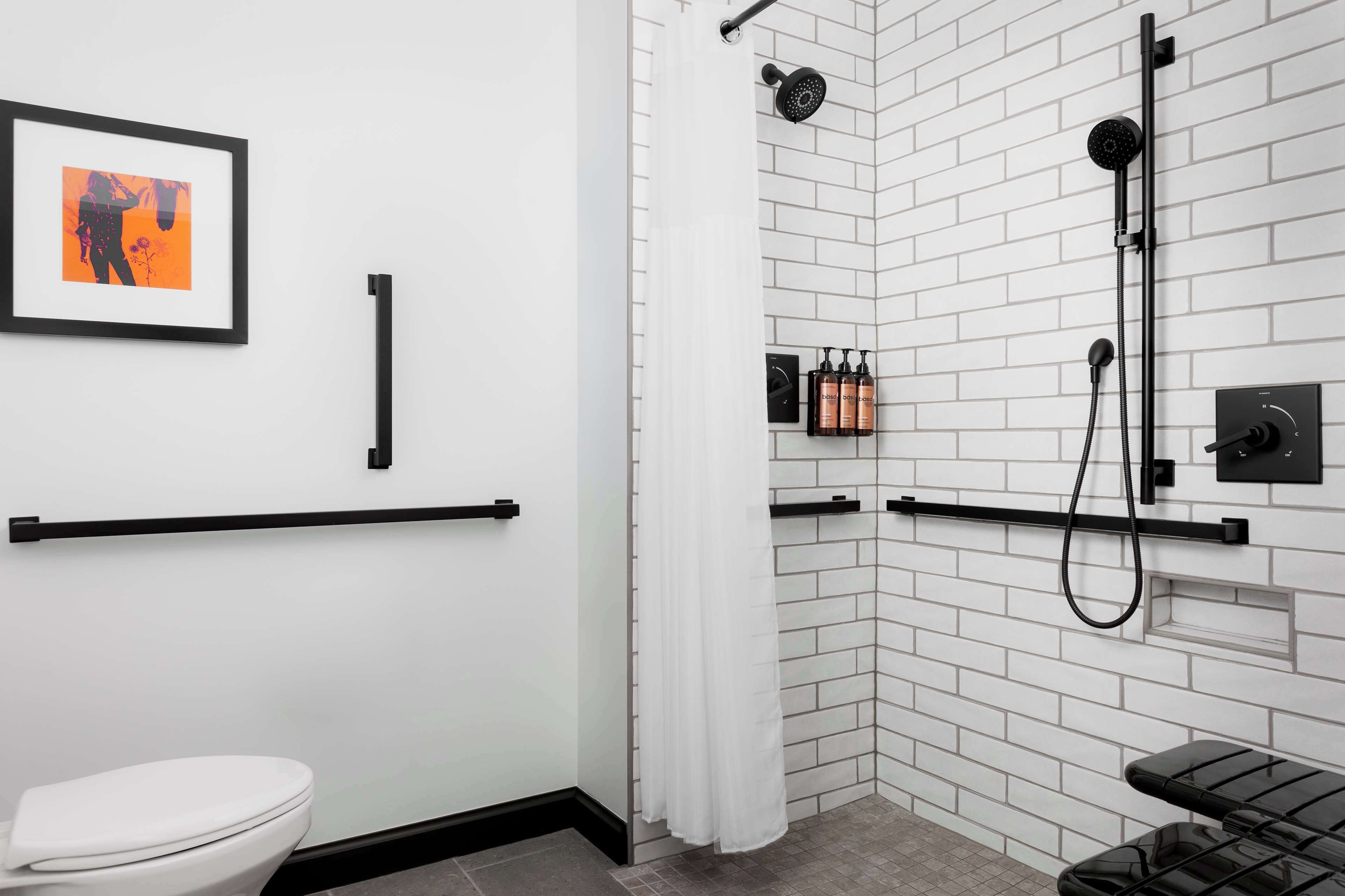 A modern bathroom with a white tiled shower, a toilet, and a framed picture on the wall.