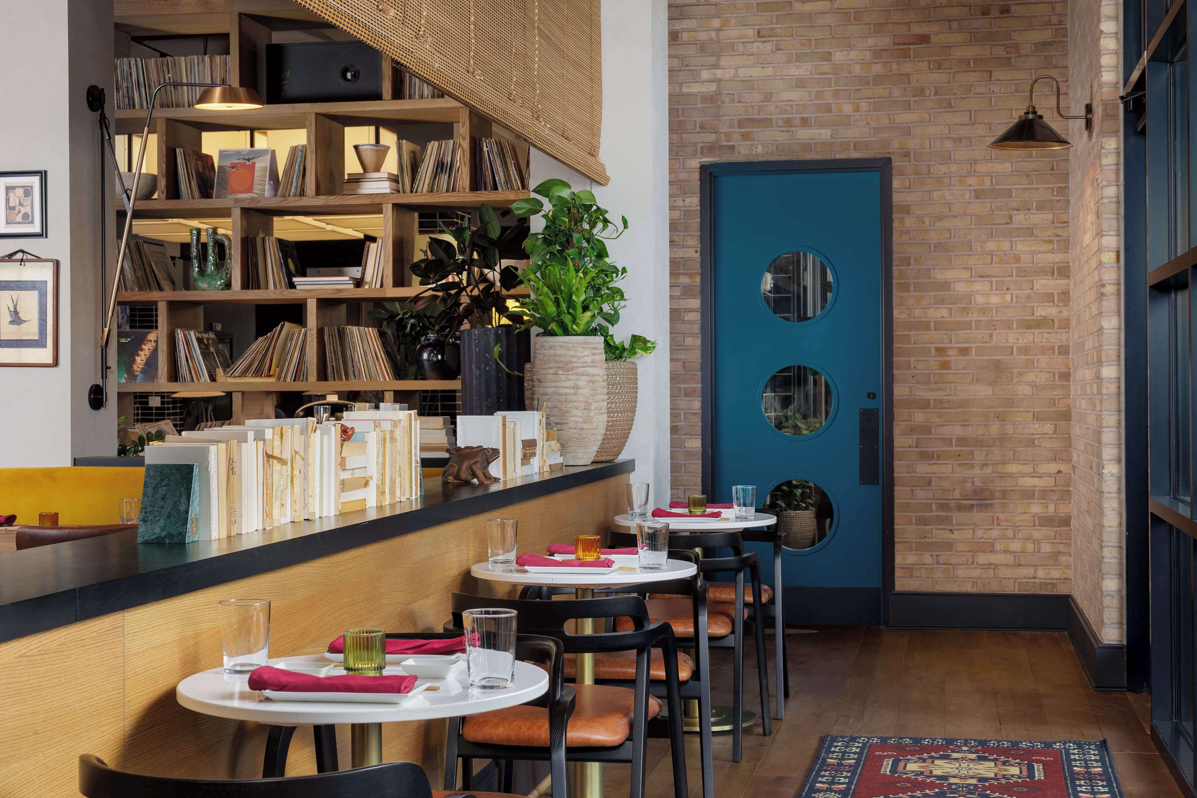 Un restaurante con mesas redondas, sillas, una estantería y una puerta azul.