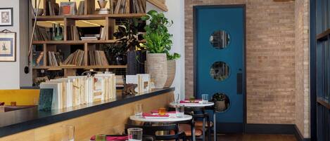 Un restaurante con mesas redondas, sillas, una estantería y una puerta azul.