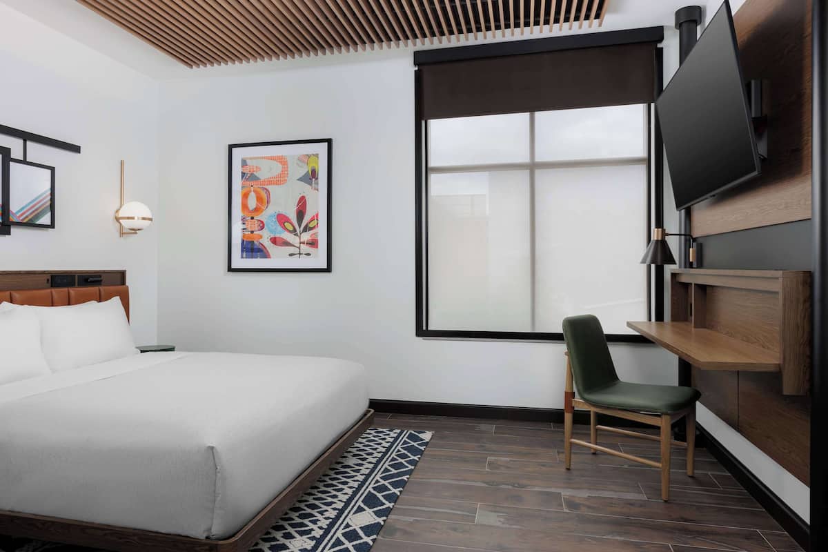 A hotel room with a bed, a chair, a TV, and a window.