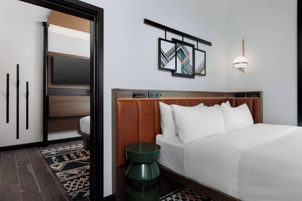 A modern hotel room with a wooden headboard, white bedding, a green side table, and a patterned rug.