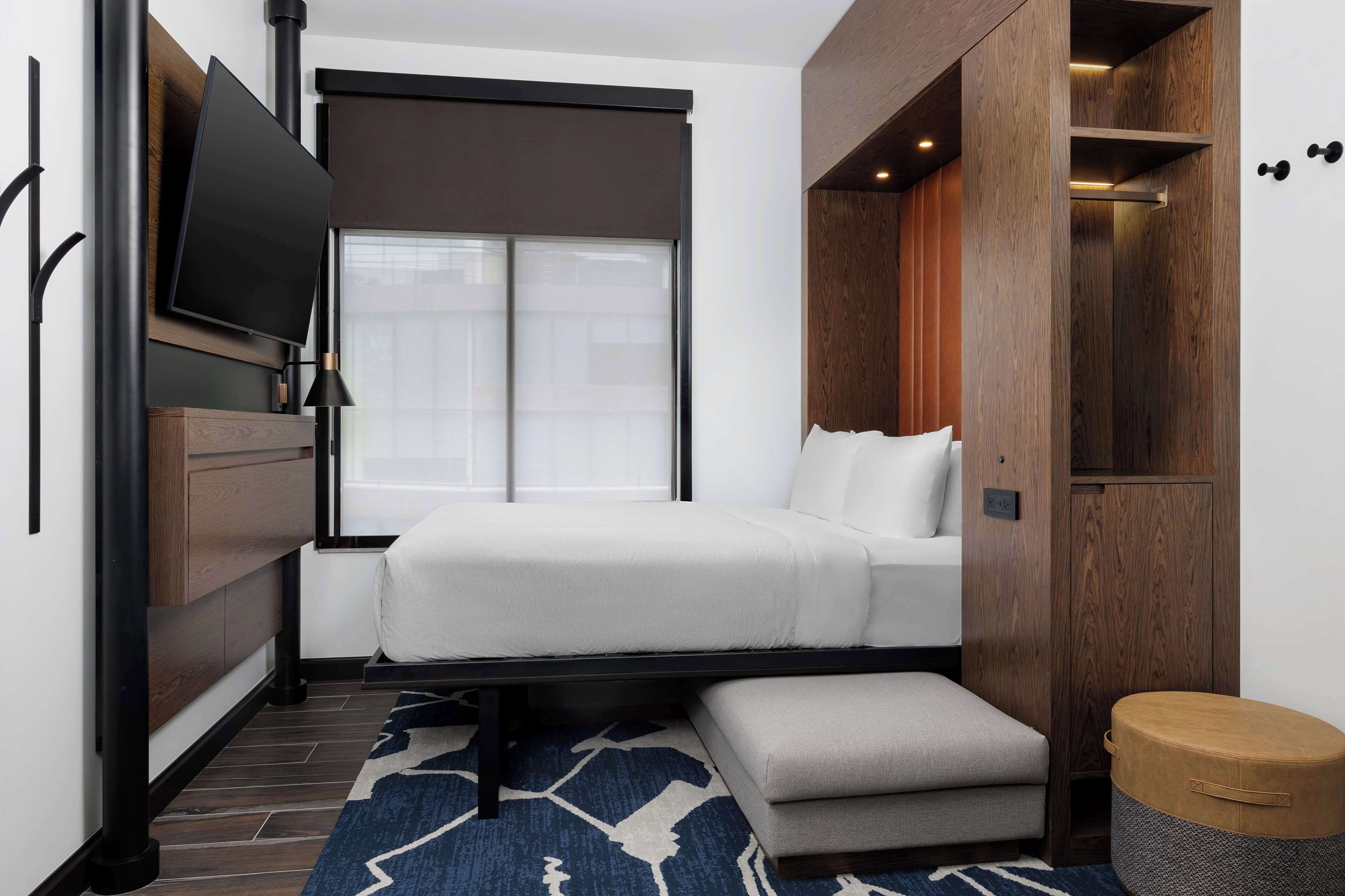 Une chambre d’hôtel de taille réduite, comprenant un lit, un petit coin salon, une télévision et une armoire.