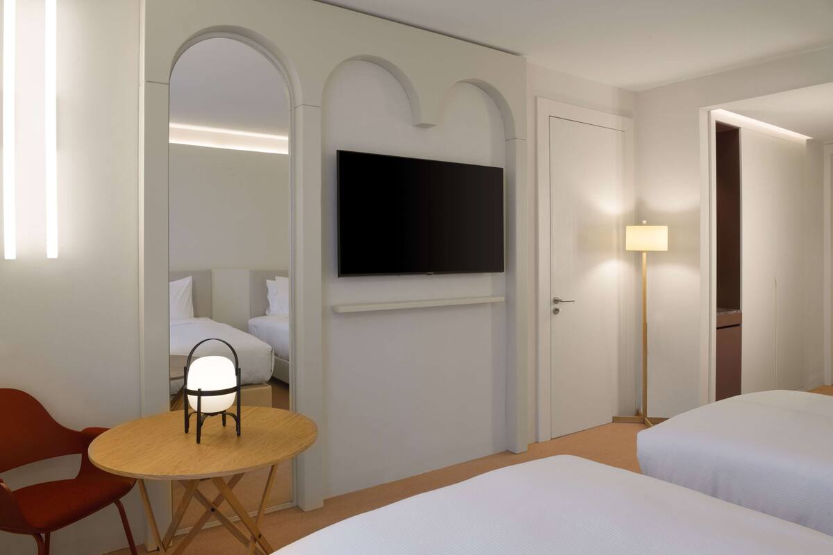 Une chambre d’hôtel équipée d’un téléviseur à écran plat fixé au mur, d’une table ronde en bois avec une chaise, de deux lits et d’une lampe.