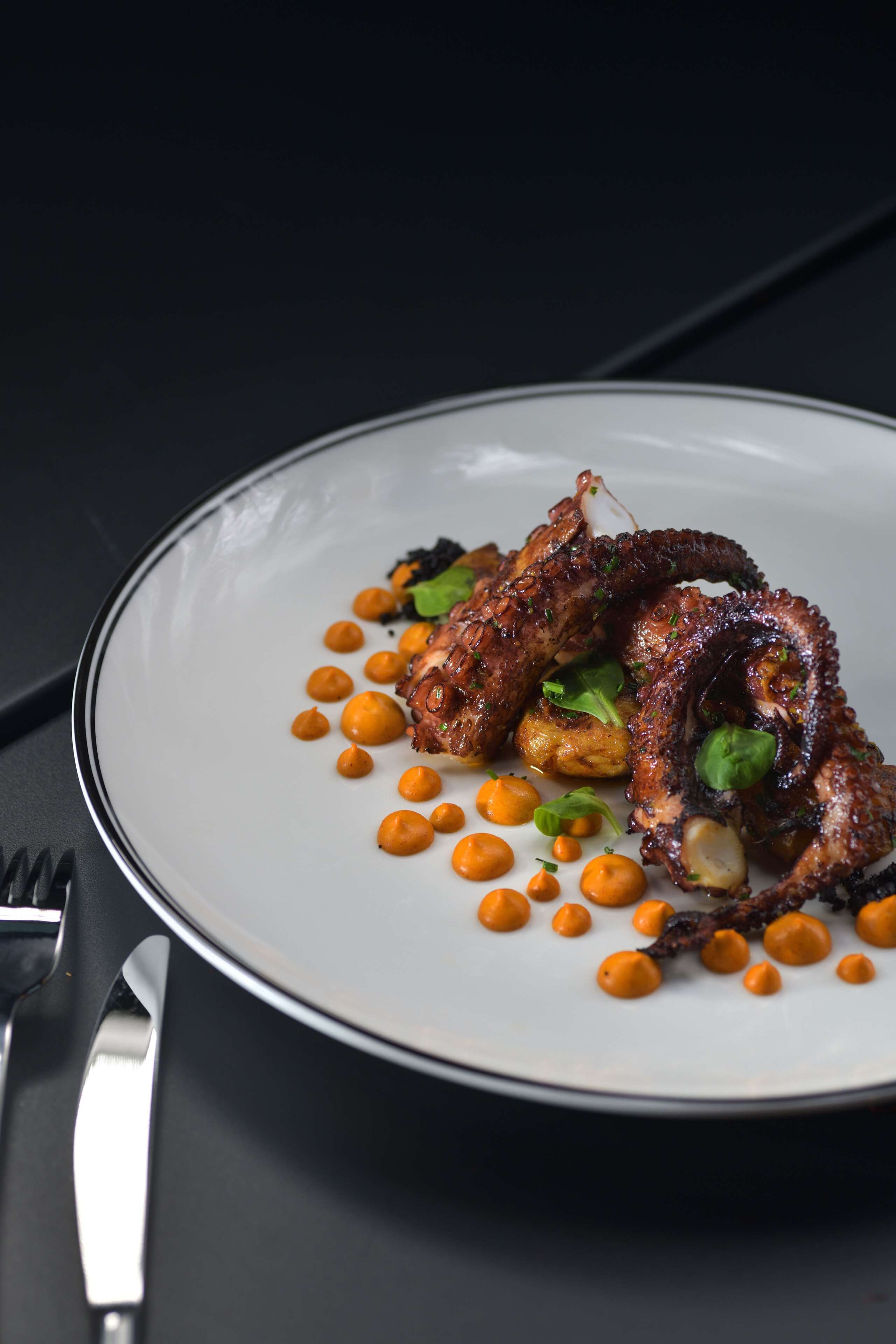 Un plato de comida con pulpo y pequeñas esferas anaranjadas, posiblemente una salsa, sobre un plato blanco.