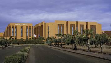 Un hotel llamado "DOUBLETREE by Hilton" con un diseño arquitectónico moderno, destacando amplios ventanales y un jardín cuidado con palmeras.