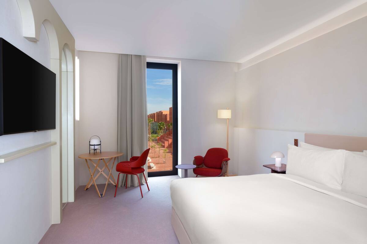 Une chambre d’hôtel comprenant un lit, une télévision, un bureau avec deux chaises, une lampe et une vue sur l’extérieur.