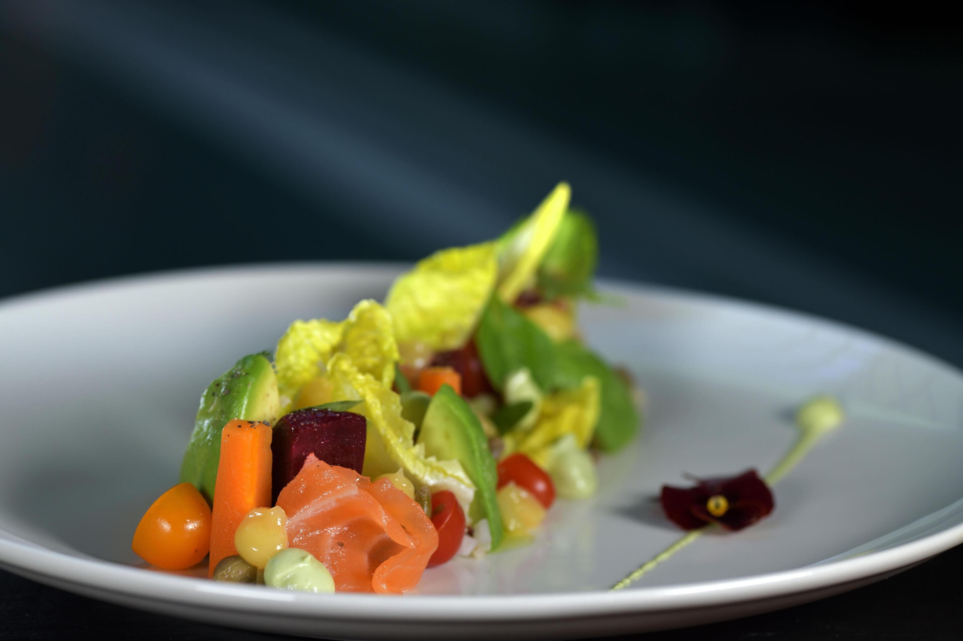 Ein weißer Teller mit einem farbenfrohen Salat, darunter Avocado, Rote Bete, Karotten und anderes Gemüse.